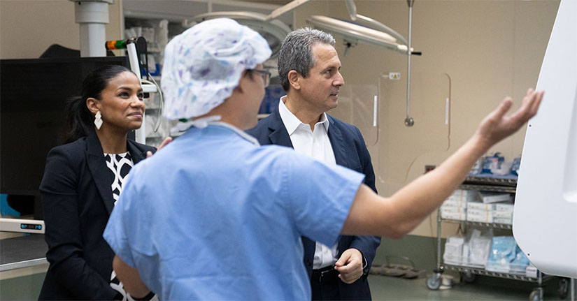 Musalem and a woman watch and listen as a man in hospital scrubs gestures to a machine.