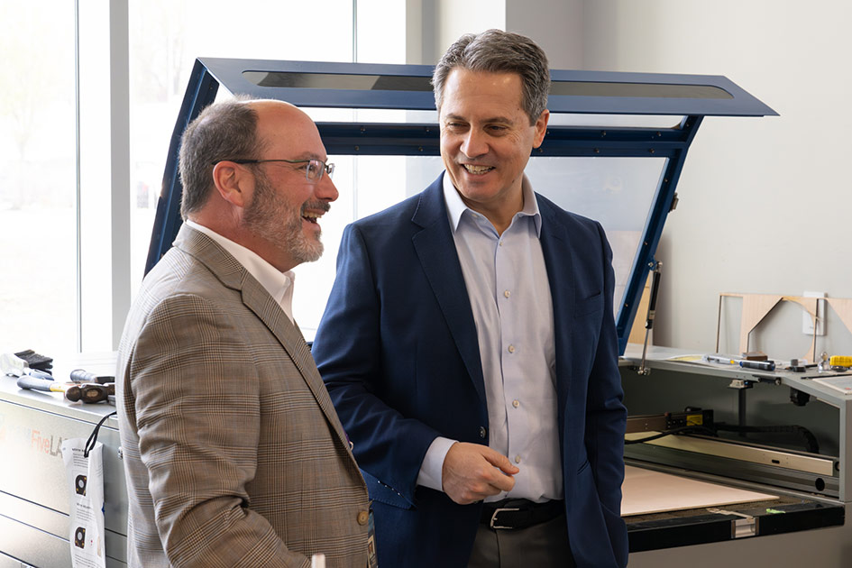 A man speaks with Musalem in front of a large laser cutter.