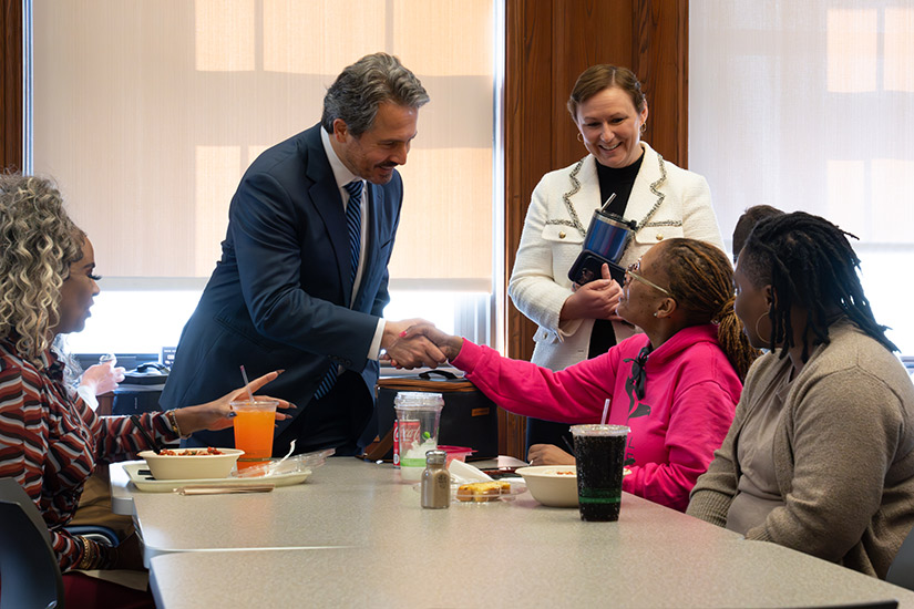 Man and woman shake hands as colleagues look on and smile.