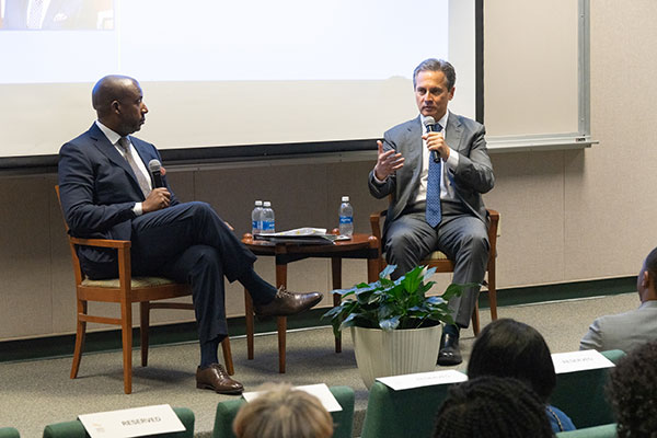 St. Louis Fed President Alberto Musalem speaks to the audience as he sits with another man on a stage.