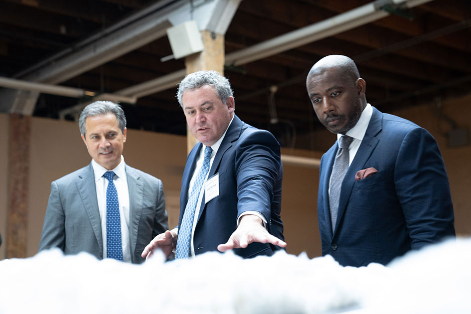 A man gestures to cotton on a table while speaking to St. Louis Fed President Alberto Musalem and another man.