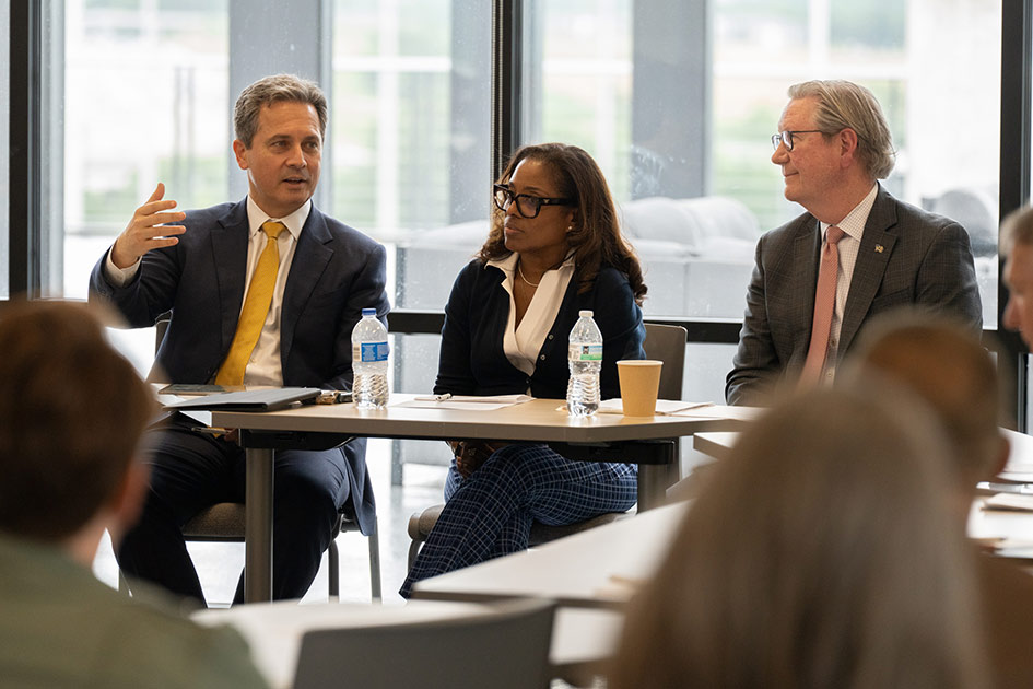 Seated at a table with a man and a woman, St. Louis Fed President Alberto Musalem gestures while speaking to a group of people.