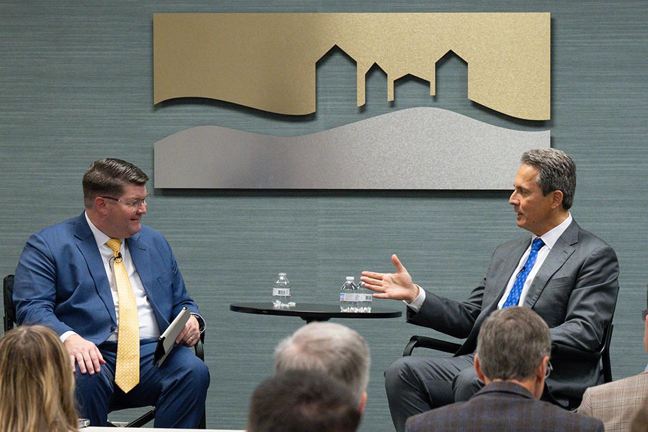 St. Louis Fed President Alberto Musalem speaks to another man as they sit on a stage in front of an audience.