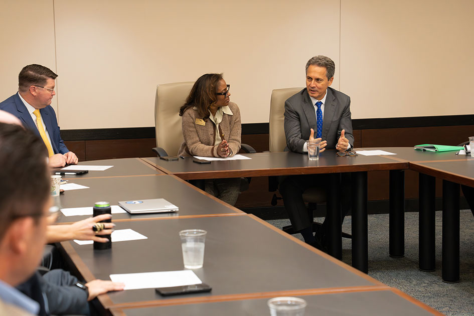 President Musalem gestures and speaks to people in business attire seated at joined conference tables.