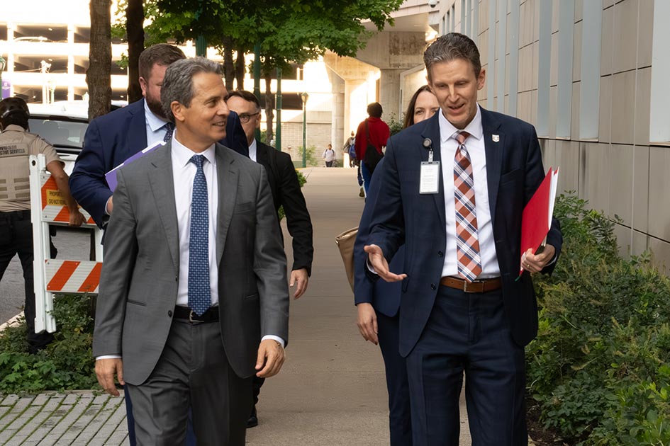 St. Louis Fed President Alberto Musalem walks on a sidewalk by a building. Another man walks alongside him and three other people follow.