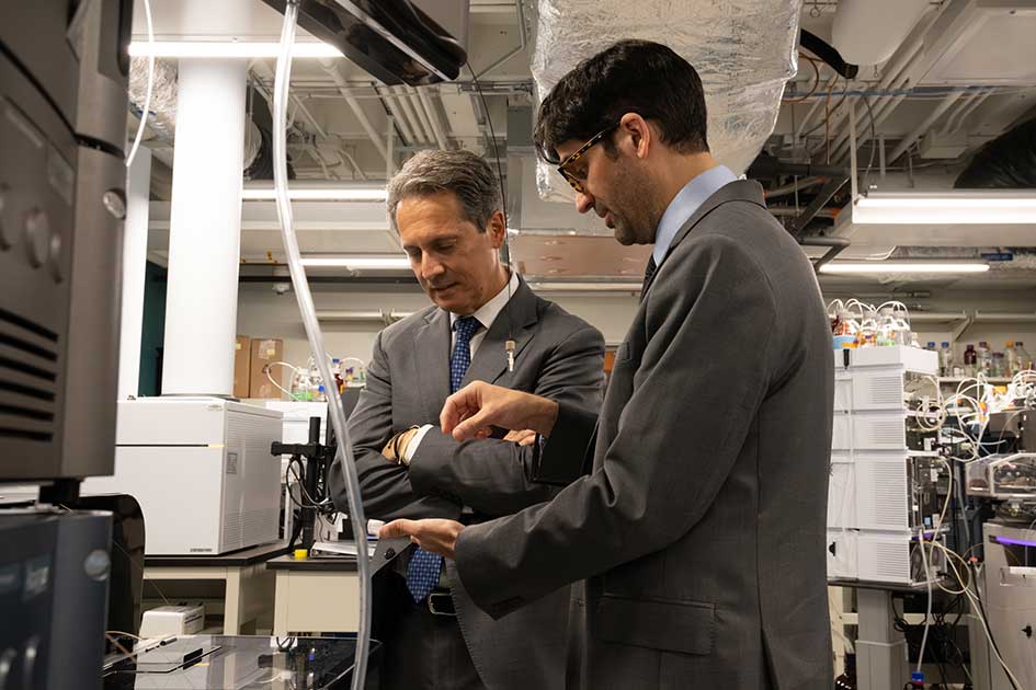 Standing in a laboratory, St. Louis Fed President Alberto Musalem watches as a man speaks and handles lab equipment.