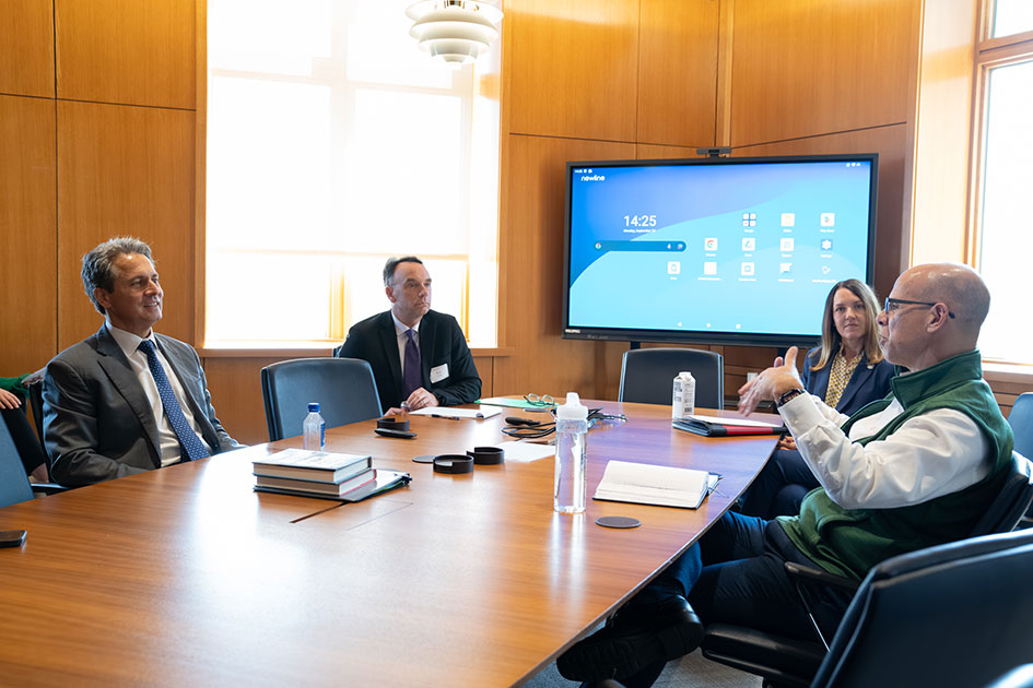 A man talks as St. Louis Fed President Alberto Musalem and a man and a woman seated with him at a conference table listen.