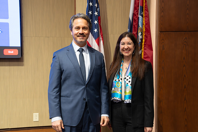 Man and woman stand in auditorium in front of two flags.