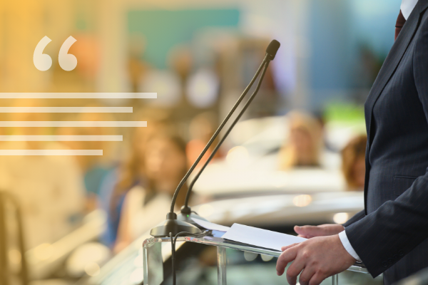 decorative image of a profile view of a person dressed in business attire standing in profile at a dais with a microphone