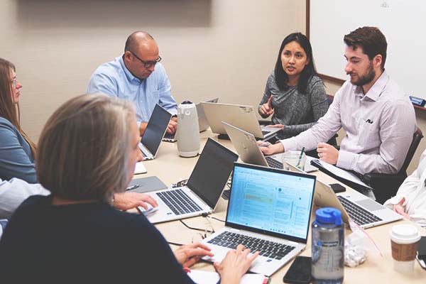 Many employees sit together in a conference room with their laptops open.