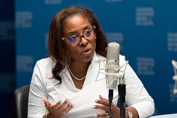 Woman in white jacket behind microphone.