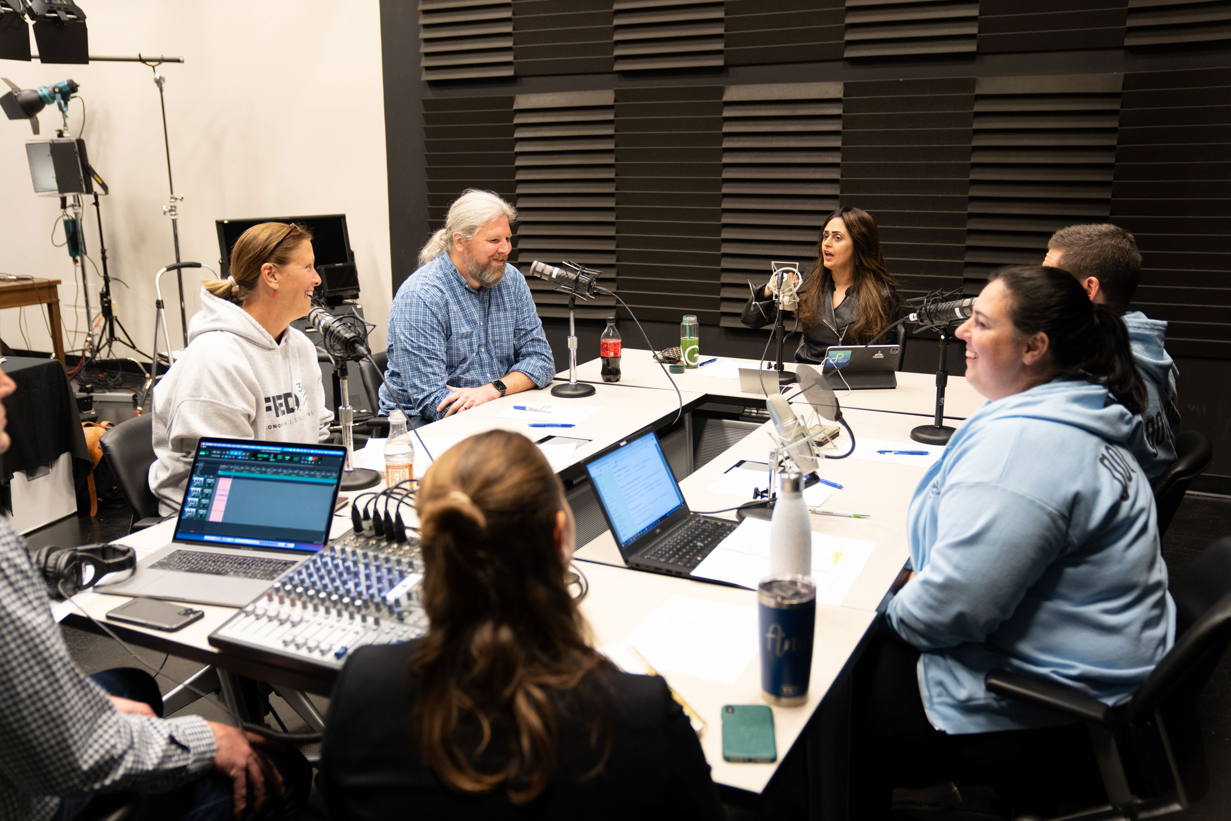 A group of individuals sit around a table recording a podcast.