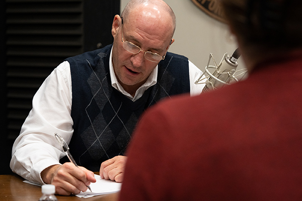 Chris Neely is sitting at a desk and taking notes during the podcast recording.