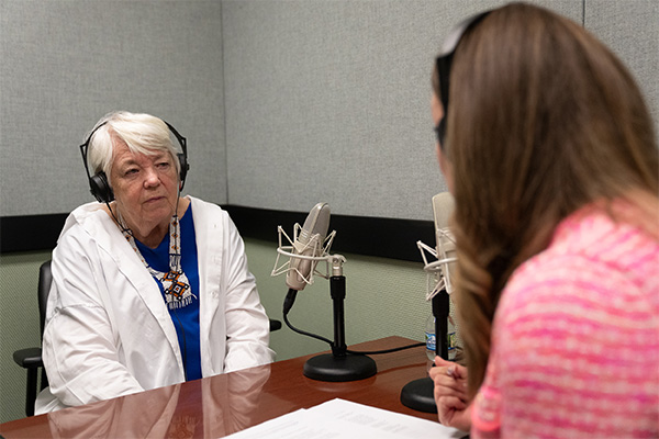 Two women with headphones sit near a portable microphone.