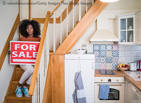 African woman sitting on stairs at home, holding a sign for sale