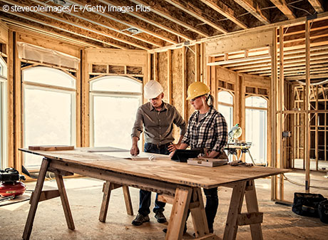 man and woman contractors at construction site looking over architectural drawings