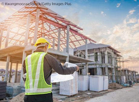 Construction worker in hard hat looking at architectural plans on a job site.