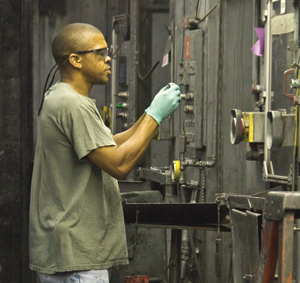 John B. McKay Jr., a Tenneco employee, performs a quality inspection on a product component made from powdered metal by a compacting press.