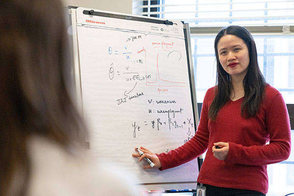 Economic research associate stands at whiteboard, discussing the labor market with a co-worker.