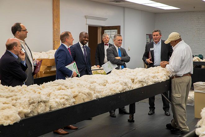 Group of men observe a worker inspecting a table stacked with cotton.