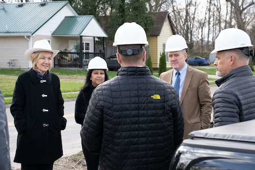 A group of people wearing hard hats converse together as they stand outside in a local community.