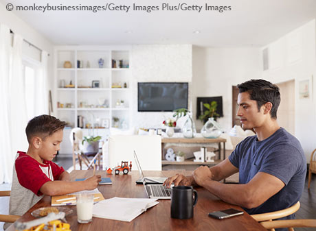 Stock photo of Hispanic father and son working opposite each other at the dining room table