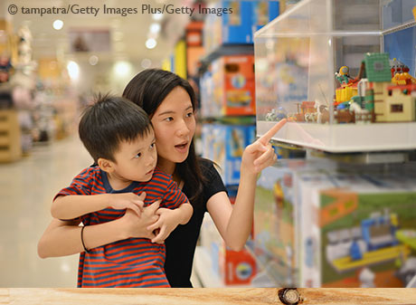 Teaching financial literacy to kids: Mom explaining purchasing decisions to young boy in a store