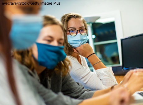 Three students wear protective masks while working on computer together.