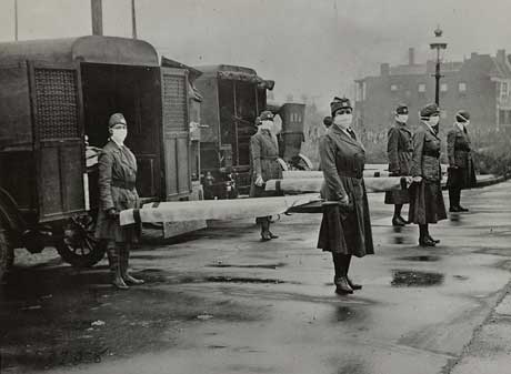 Mask-wearing women hold stretchers at the backs of ambulances.