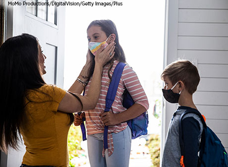 A mother helps her children put on protective masks before they leave the house to attend school.