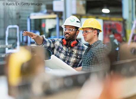 Two men with hard hats reviewing plans in a warehouse